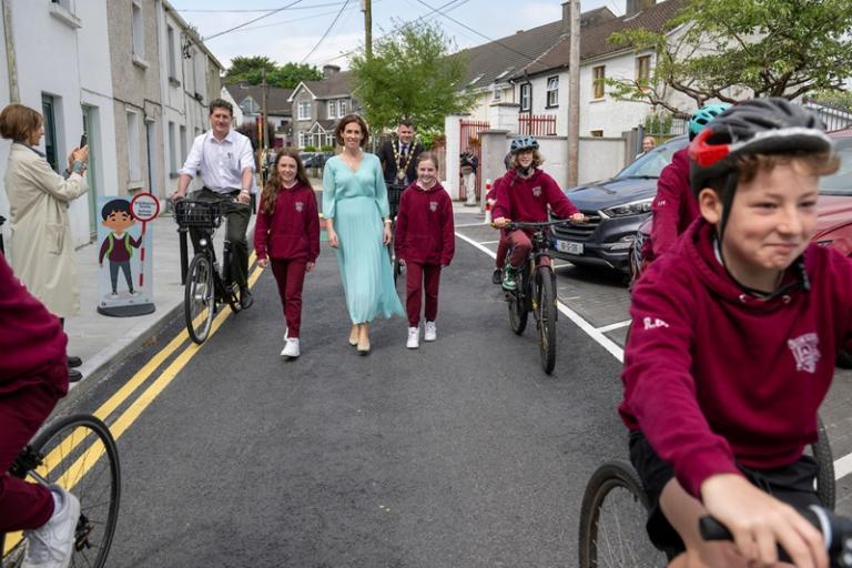 A group of children and politicians cycle and walk on the road outside of Scoil Iognáid during its launch in May 2024.